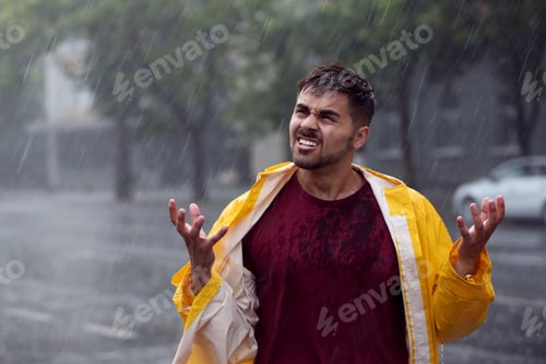 Preview: Angry young man in bright coat outdoors on rainy day