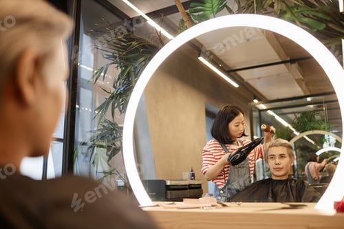 Preview: Mirror Reflection of Hairstylist Drying and Styling Hair in Beauty Salon