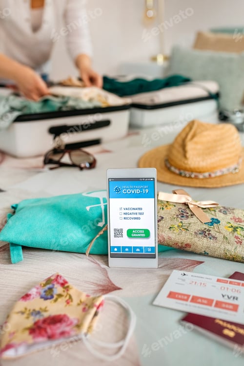 Preview: Mobile phone with covid passport with unrecognizable woman preparing suitcase for vacation