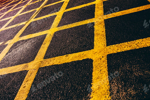Preview: Angled closeup shot of a yellow, painted, grid road mark on black asphalt