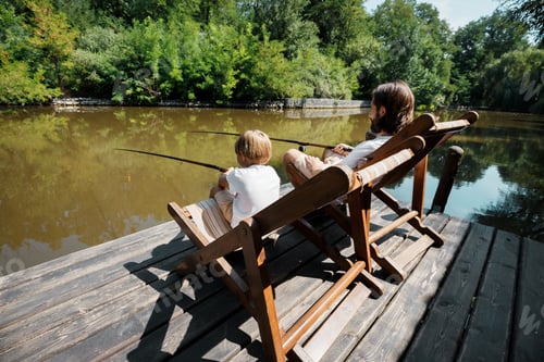 Preview: Young dark-haired father and his little son are sitting in recliners on the wooden pier with fishing