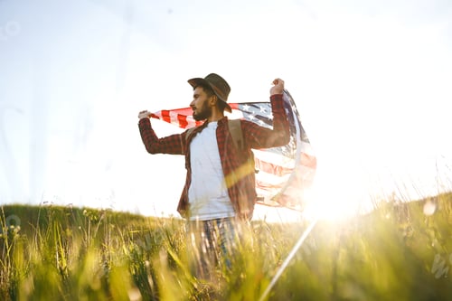 Preview: 4th of July. American Flag. Traveler with flag of America. Man in hat, backpack, a shirt and jeans.