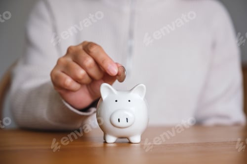 Preview: Closeup image of a woman putting coins into piggy bank for saving money concept