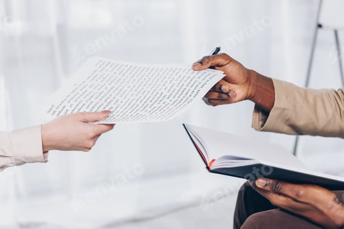 Preview: Cropped view of african american employee with notebook giving papers to recruiter in office