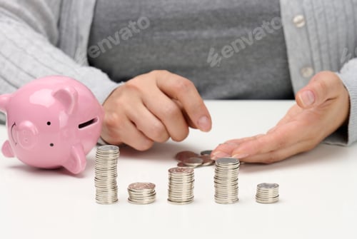 Preview: Stack of metal coins and a ceramic pink piggy bank. Man counting money