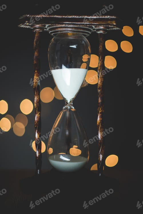Preview: Vertical closeup shot of a sand glass clock with blurred lights in the background