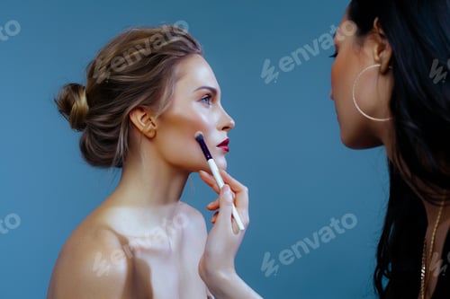 Preview: Makeup artist applies blush with brush to face of beautiful blonde on blue background