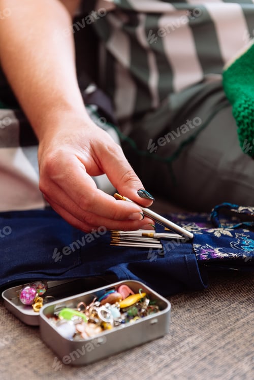Preview: Crop of male hands with manicure grabing knitting supplies on sofa