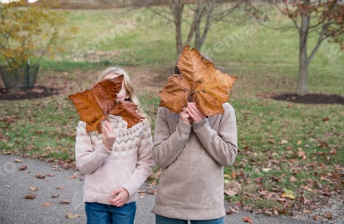 Preview: Two children each holding up a large maple leaf over their face