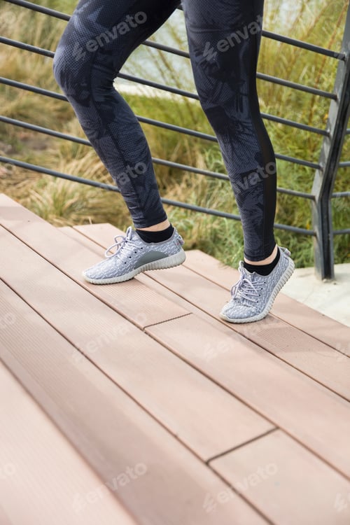 Preview: Legs of the sporty female runner athlete going up stairs in urban city