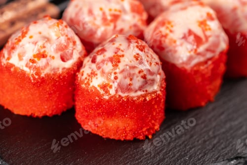 Preview: Sushi roll with mayonnaise sauce and red tobiko caviar served on black board and soy sauce.