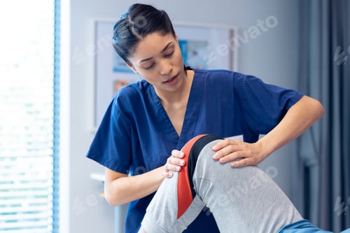 Preview: Smiling diverse female physiotherapist treating knee of senior male patient in therapy, copy space