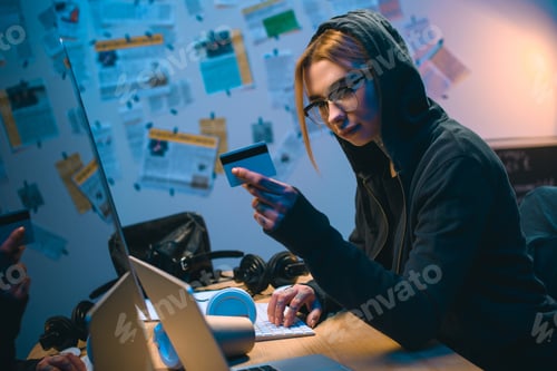 Preview: young female hacker with stolen credit card working with computer