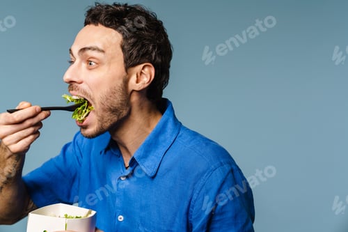 Preview: Excited handsome hungry guy eating salad takeaway