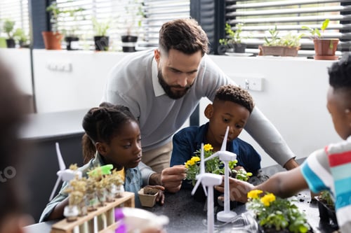 Preview: Diverse elementary schoolchildren and male teacher studying plants together in school class