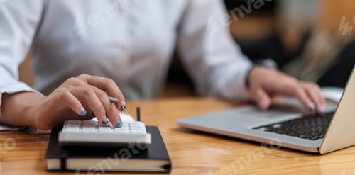 Preview: Close up Business woman using calculator and laptop for do math finance on wooden desk in office and
