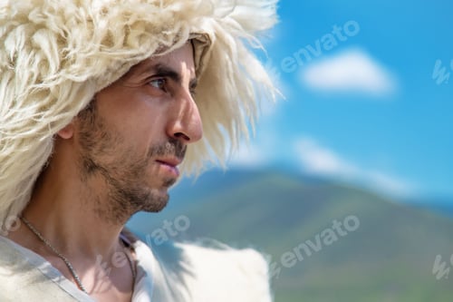 Preview: A Georgian man in a hat against the background of mountains and the sky. Selective focus.