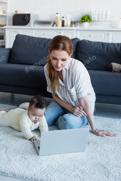 Preview: mother sitting on floor near african american baby girl and laptop