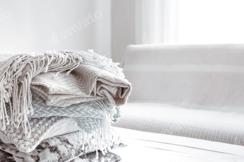 Preview: Close up of a stack of cozy Scandinavian style blankets and pillows copy space.