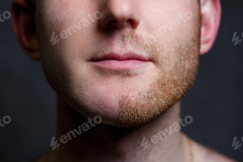 Preview: Young man shaving his beard. He shaved off half the bristles against a gray background