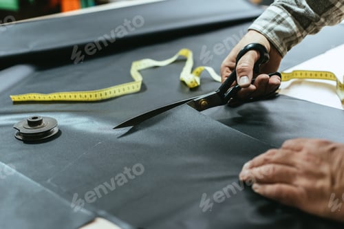 Preview: cropped image of male handbag craftsman cutting leather by scissors at workshop