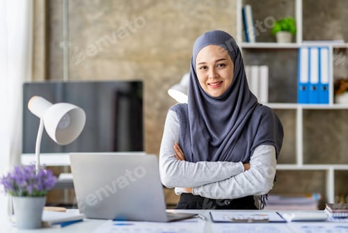 Preview: Attractive Muslim woman wearing hijab looks at camera working in business office. Use a calculator a
