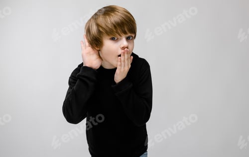 Preview: Charming teenager with blond hair and dark eyes. The boy closes his mouth with one hand, brings his