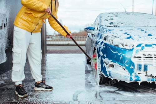 Preview: a girl in a yellow jacket with a brush washes a wheel at a self-service car wash
