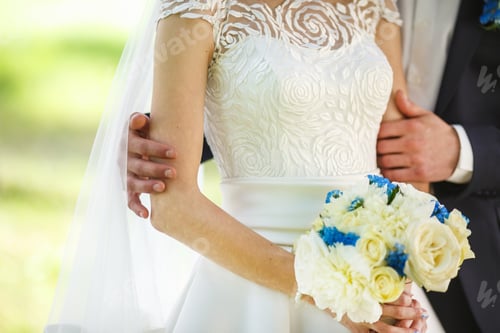 Preview: groom embraces the bride with wedding bouquet. the hands of the newlyweds