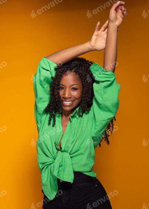 Preview: Studio portrait of a cheerful Hispanic woman dancing with arms raised on a yellow background