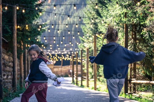 Vista previa: Two little girls dance in the forest on a blurred background with light bulbs.