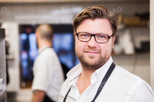 Preview: Portrait of confident chef at commercial kitchen with colleague in background