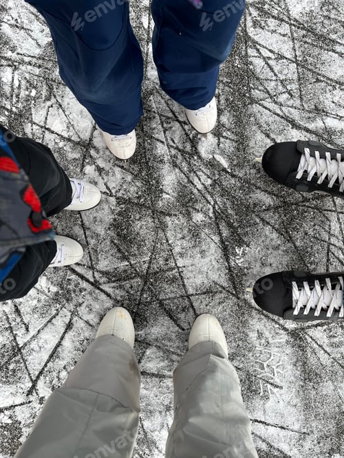 Preview: feet in ice skates on rink ice. a family of four with children goes ice skating in winter. top view