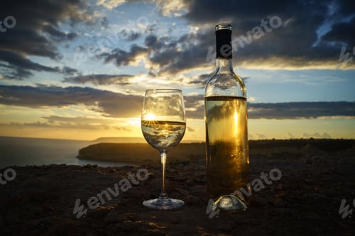 Preview: Bottle and glass of white wine against a breathtaking seaside sunset