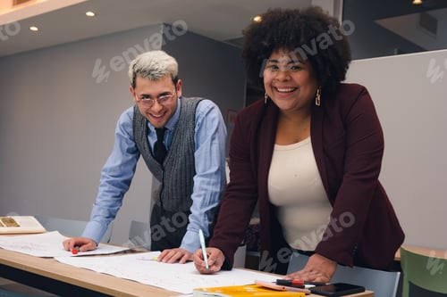 Preview: Business Man and Woman at work laughing looking at the camera while making sketches at the table