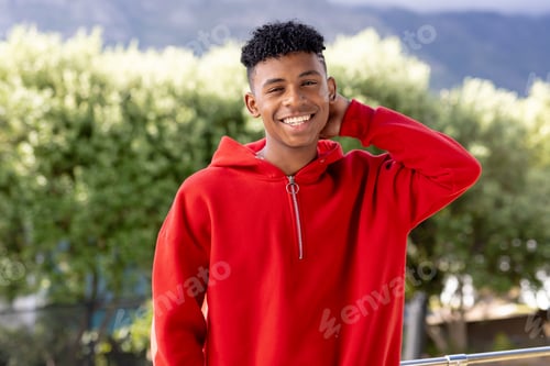 Preview: Image of smiling biracial man in red hooded top with copyspace over trees in background
