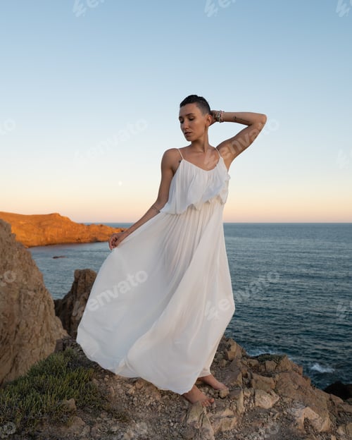 Preview: Young woman in a white dress standing on a cliff, enjoying a sunset