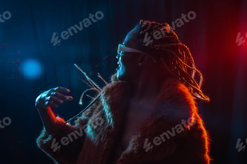 Vorschau: Schwarze ethnische Frau mit Zöpfen mit blauen und roten LED-Lichtern, die Spaß hat und auf einer Party tanzt