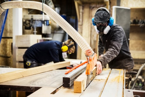 Preview: Man wearing ear protectors, protective goggles and dust mask standing in a warehouse, cutting piece