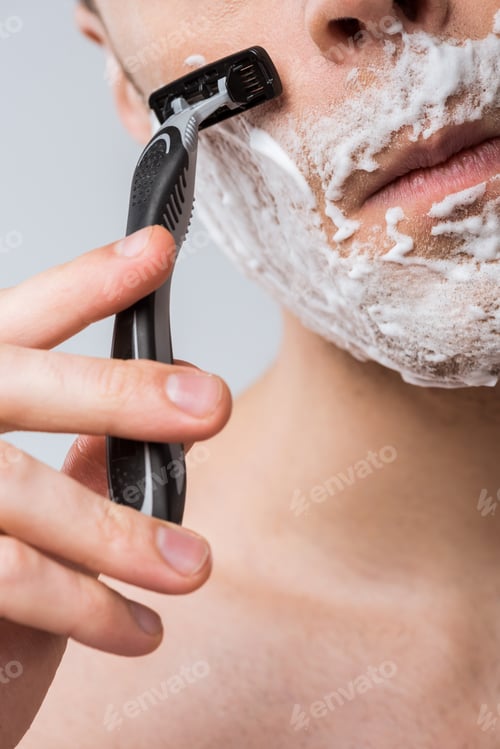 Preview: cropped view of young man foam on face shaving with razor, isolated on grey