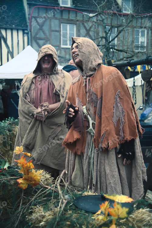 Preview: Men wearing traditional Medieval attire engaged in conversation near a historical stone building