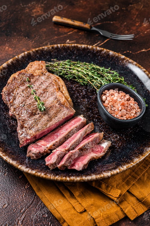 Preview: BBQ roast sliced New York beef steak on a plate with thyme and salt. Dark background. Top view