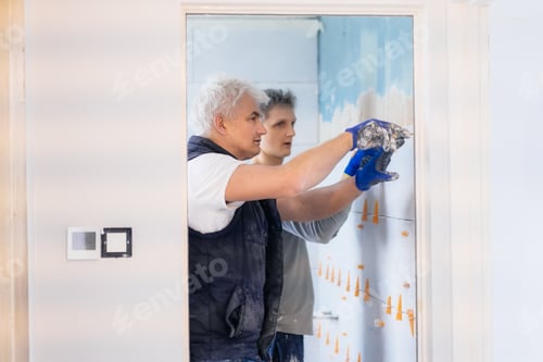 Preview: Father and son laying tiles on a bathroom wall. DIY concept. House improvement