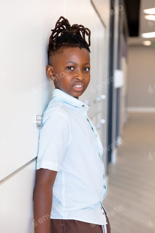 Preview: Portrait of african american elementary schoolboy standing by locker in school