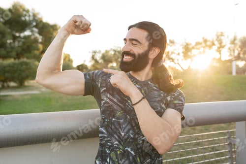 Preview: Handsome bearded man with long hair standing, strong athlete showing arm muscle,