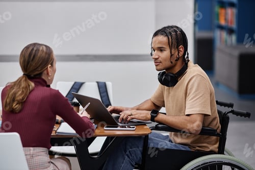 Preview: Young black boy with disability studying in college library with friend