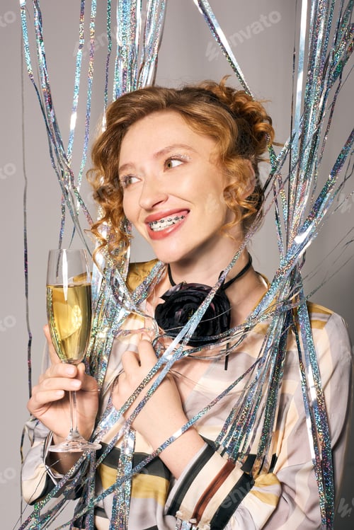 Preview: Young woman joyfully celebrating with champagne while surrounded by colorful streamers