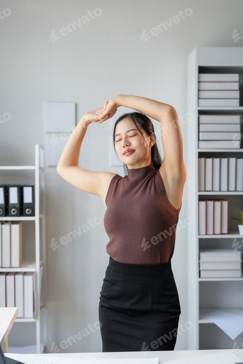 Preview: Young asian businesswoman is stretching her arms at office desk