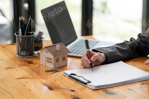 Preview: Cropped image of woman hand holding pen writing on blank paper with house model and keys.