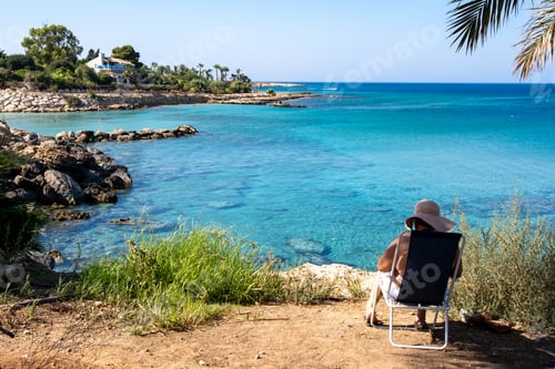 Preview: woman sitting on a chair relaxing and reading a book during summer holidays at the beach with